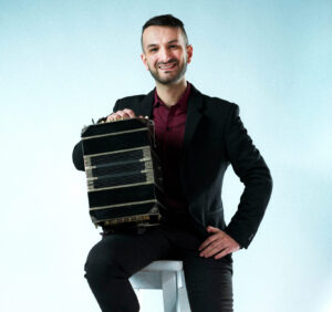 Alejandro Pereyra sentado en un banco con su bandoneon, retrato de estudio